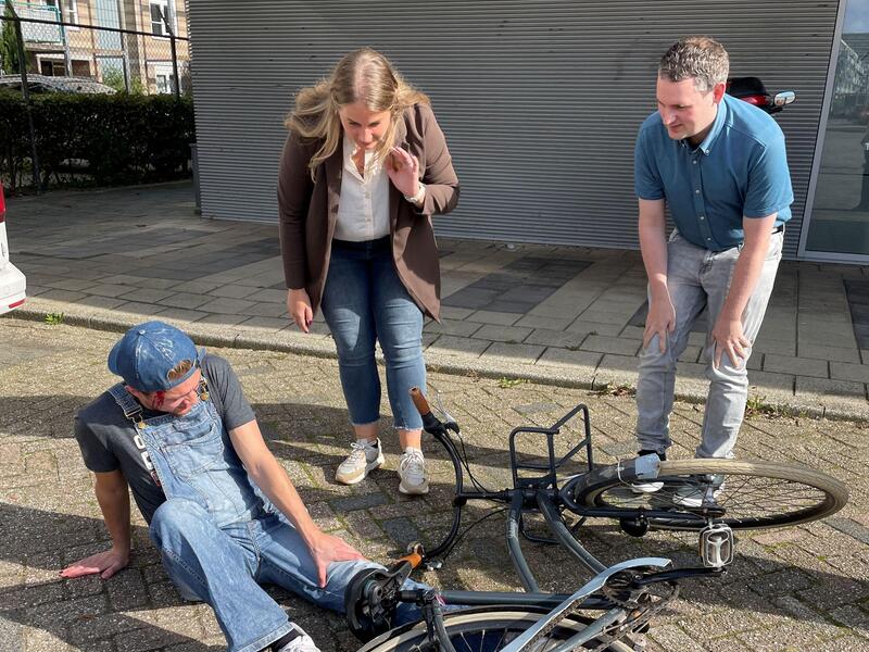 man op grond met fiets op hem man en vrouw staan erbij