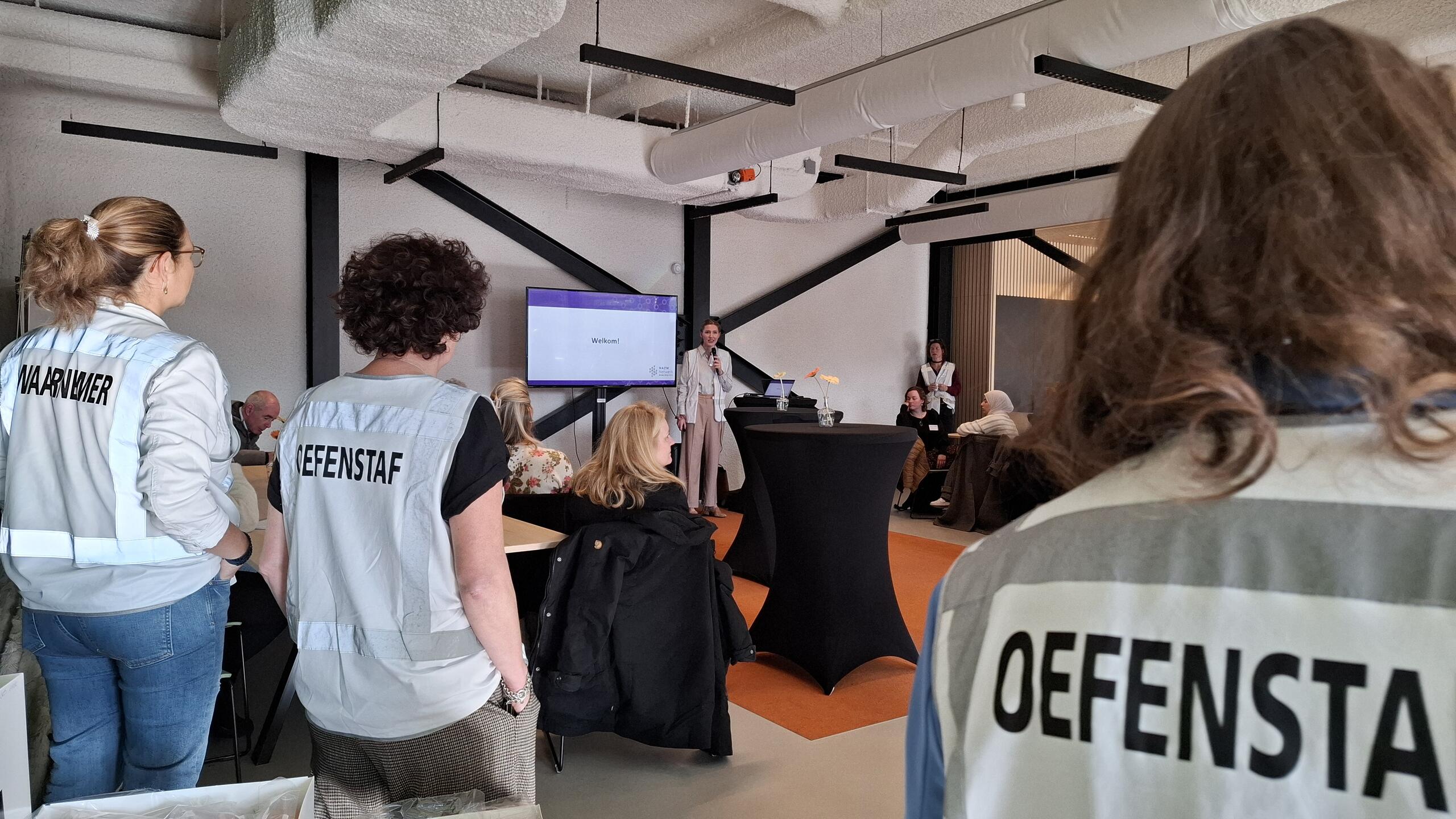 Mensen in grote ruimte bij bijeenkomst, oefenstaf op de rug gekeken
