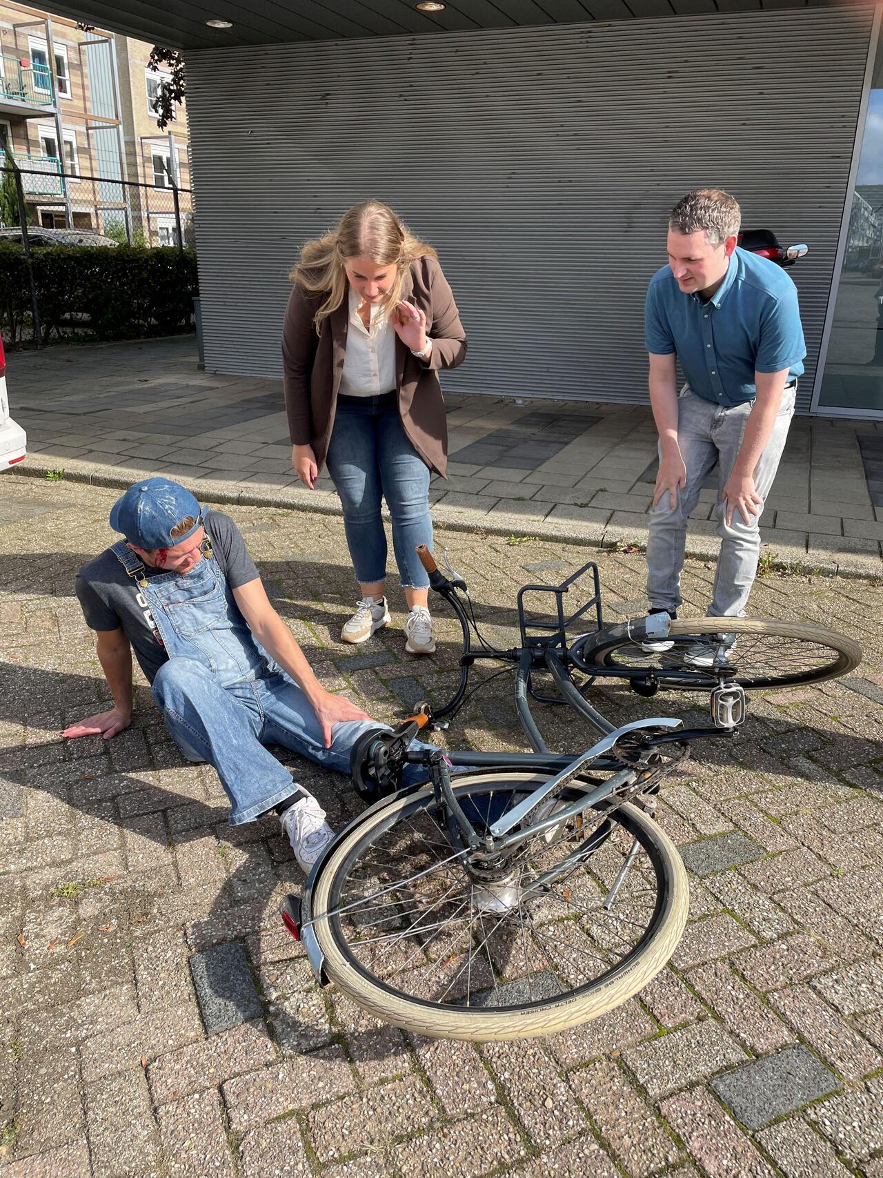 man op grond met fiets op hem man en vrouw staan erbij