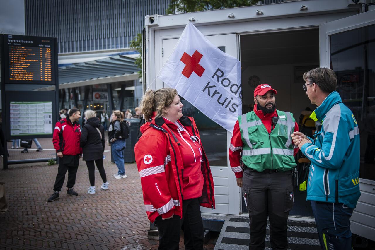 Officier van Dienst Geneeskundig in gesprek met twee Rode Kruis medewerkers buiten vlag Rode Kruis zichtbaar