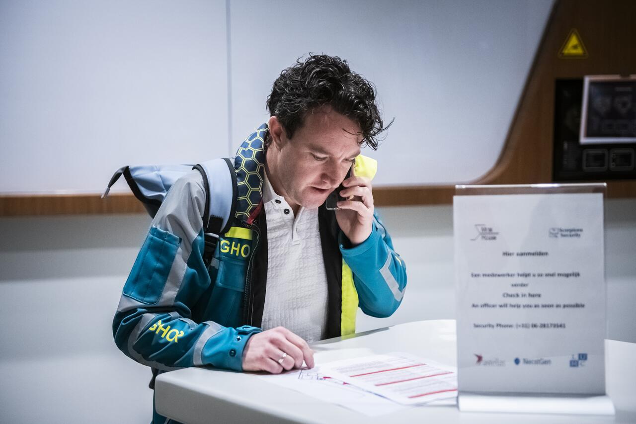 GHOR crisisfunctionaris staat te bellen terwijl hij kijkt op papier met informatie