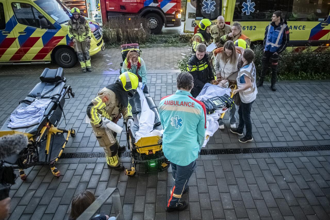 Slachtoffer op brancard gedragen door mensen van de ambulance op straat, op achtergrond twee ambulances