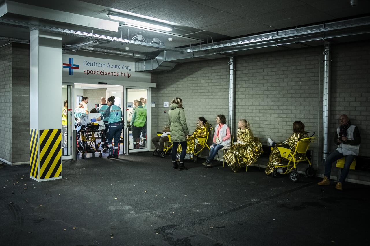 Slachtoffers in rij op stoelen voor ingang spoedeisende hulp, slachtoffer wordt op brancard naar binnen gebracht